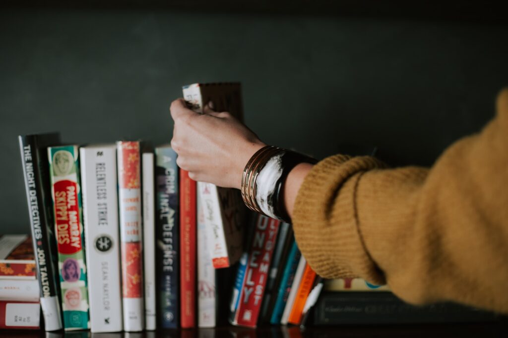 woman wearing bracelets selecting a book from the colourful bookshelf